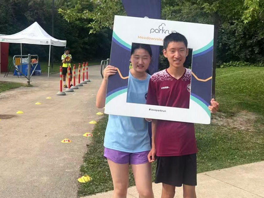 Two youth smiling behind a Meadowvale parkrun photo frame at the community parkrun event